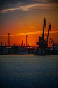 Cranes by sea against sky during sunset