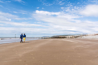 Rear view of couple walking at ynyslas beach against sky
