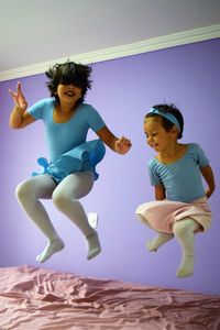 Full length of sisters jumping on bed at home