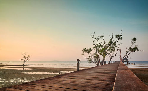 Wooden pier at beach against sky during sunset 