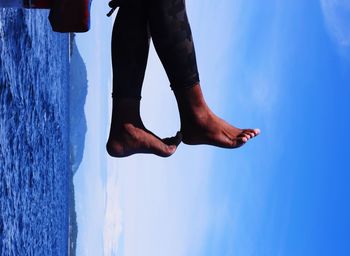 Low section of man standing by sea against blue sky