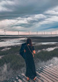 Rear view of woman standing on boardwalk against sky