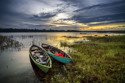 Boat moored on shore against sky during sunset