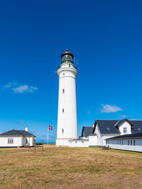 Lighthouse by building against clear blue sky
