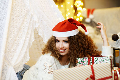 Pretty woman laying on christmas giftboxes wear santa hat on bokeh lights background in home room