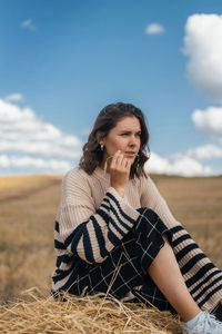 Beautiful young woman sitting on field against sky