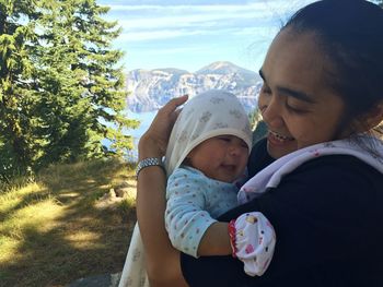 Side view of smiling mother carrying cute baby girl on field