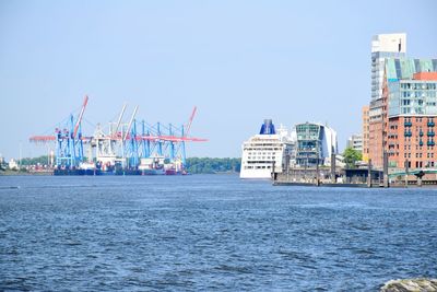 Cranes by sea against buildings in city against sky