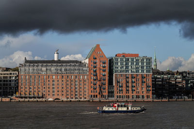 Buildings by river against sky in city