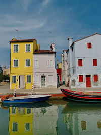 Boats moored in canal by buildings against sky