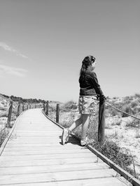 Side view of woman on wooden structure against sky