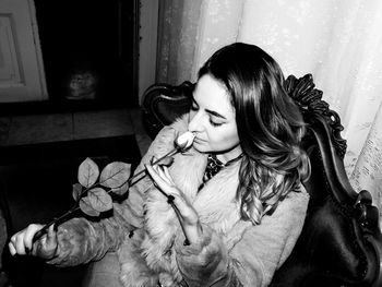 Young woman smelling flower while sitting at home