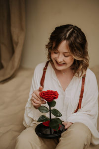 Young female in victorian shirt sitting with rose on the sand and smile