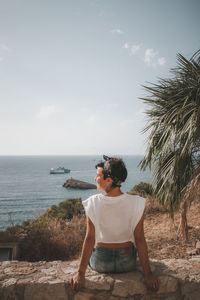 Rear view of woman sitting on retaining wall against sea