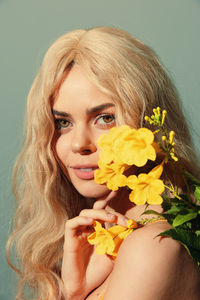 Close-up of young woman holding yellow flower against wall