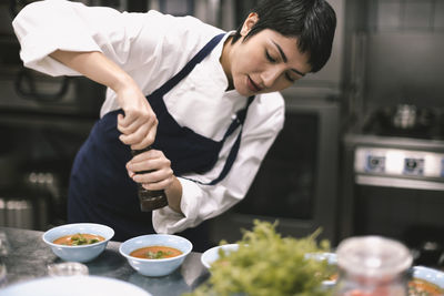 Female chef adding pepper in soup at kitchen counter in restaurant