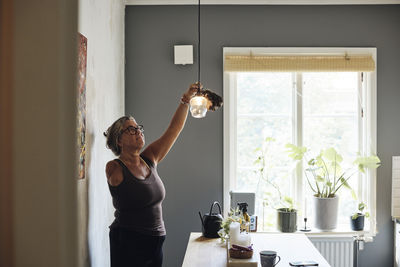 Mature woman with disability cleaning light while standing at home