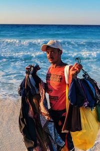 Man selling stuff at beach against sky