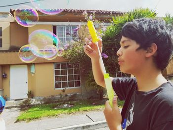 Side view of teenage boy blowing bubble while standing on street