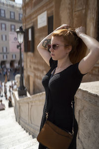 Ginger woman with sunglasses is straightens her hair in sunlight