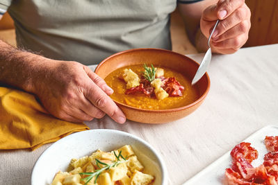 Man eating pumpkin cream soup with roasted bacon and croutons in clay plate on the table