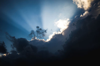 Low angle view of sunlight streaming through clouds