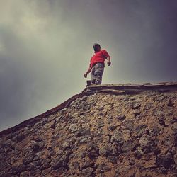 Low angle view of man standing on roof against sky