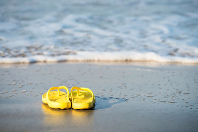 Close-up of yellow flipflop shoes on beach