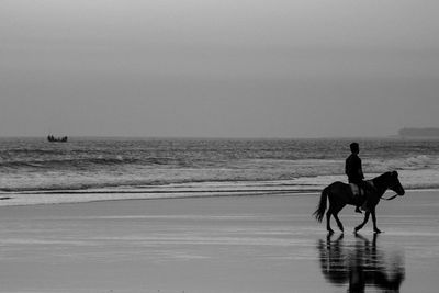 Silhouette people riding on beach against clear sky