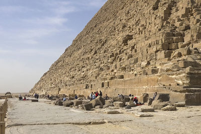 Low angle view of tourists on rock against sky