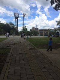 Footpath in park against cloudy sky