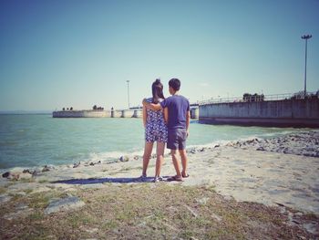 Rear view of friends standing on beach against clear sky