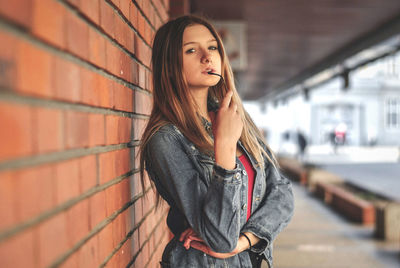 Portrait of beautiful young woman standing by brick wall