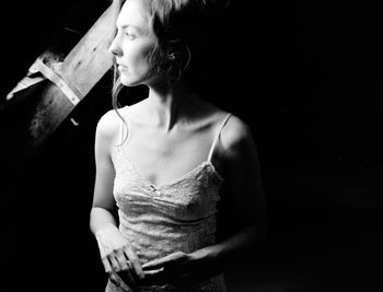 Thoughtful young woman looing through window while standing in darkroom