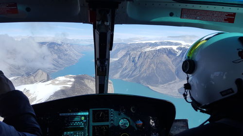 Rear view of men in helicopter flying over river and mountains in winter