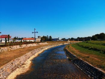 Road amidst field against clear blue sky