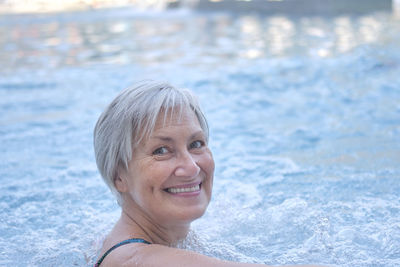 Smiling senior woman with gray hair looking at camera in outdoor thermal pool with hydromassage. 
