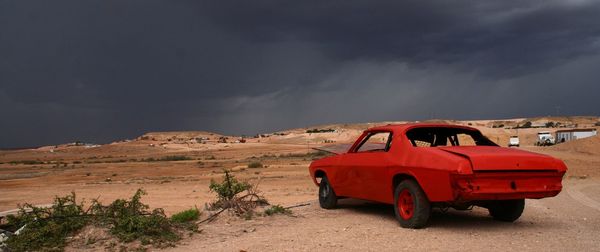 Red car on desert against sky