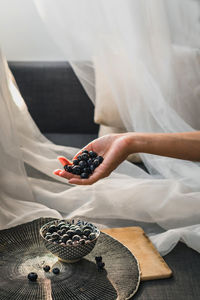 A woman's hand holding blueberries. underneath is a little bowl with more blueberries.