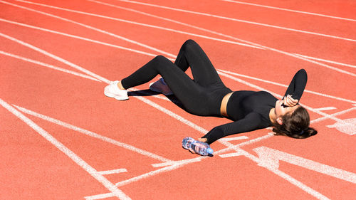 High angle view of tired woman lying with water bottle on running track