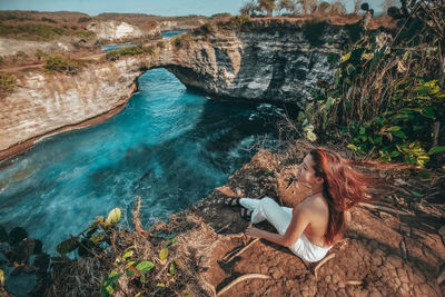 Woman sitting on rock by water