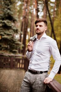 Young man looking away while standing by railing against trees in forest