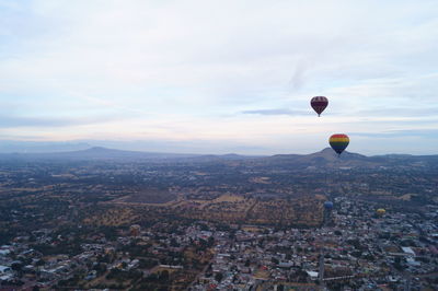 Hot air balloons flying over cityscape against sky