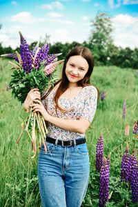 Portrait of woman holding lupine flowers while standing on field