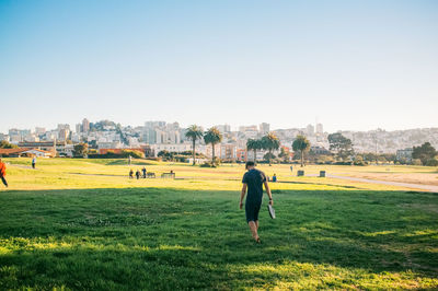 People walking on grassy field against clear sky