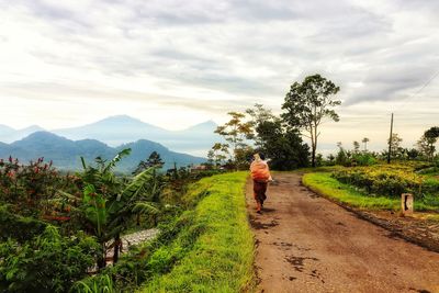 Rear view of woman walking on dirt road