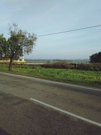 Road by trees on field against clear sky