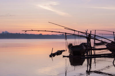 Silhouette fishing net on sea against sky during sunset