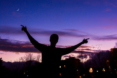 Silhouette man standing with arms outstretched against cloudy sky at dusk