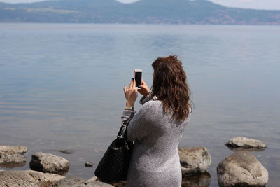 Rear view of woman photographing with mobile phone at beach